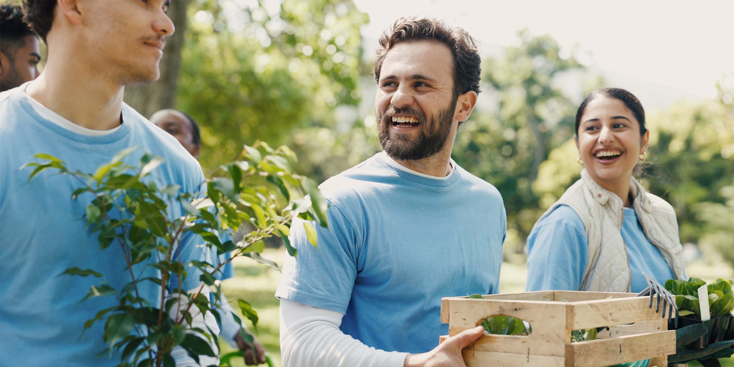 Three people in blue t-shirts carry small plants while conversing at a community fundraising event, representing BankNewport's philanthropic banking mission, charitable giving programs, and commitment to Rhode Island business and community support.
