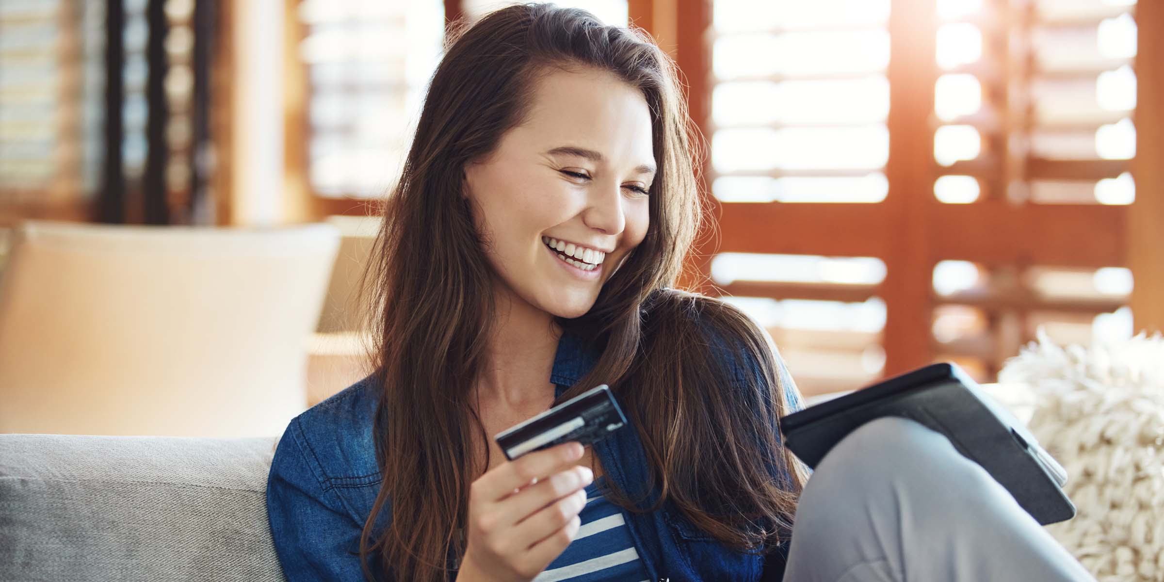 A person holding a credit card looks at a tablet displaying a personal banking interface, representing the process of opening a personal checking account online.