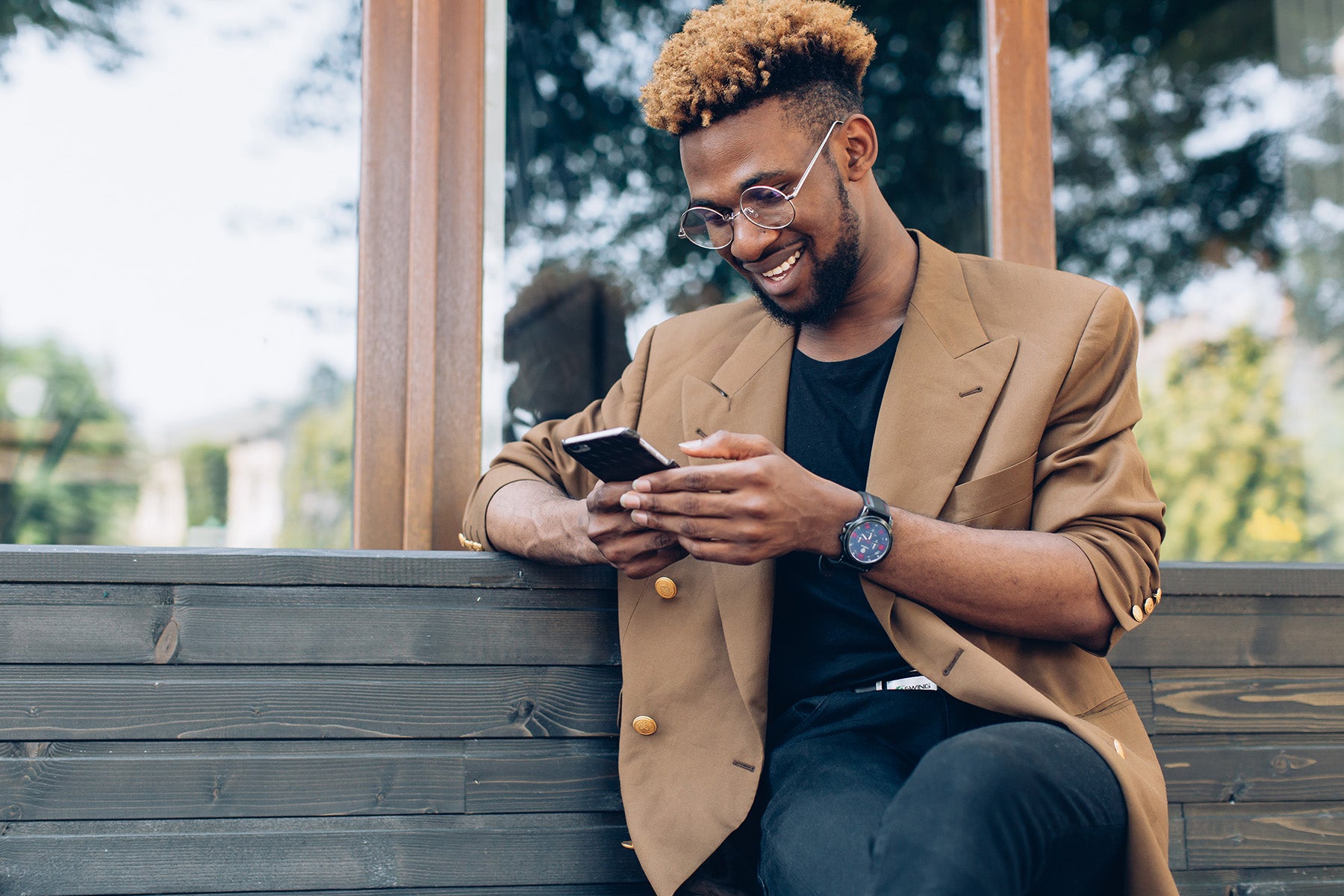 A person sits on an outdoor park bench on a sunny day, smiling contentedly while texting on their cell phone, illustrating the ease and convenience of opening a live chat with BankNewport to get banking help anytime, anywhere.