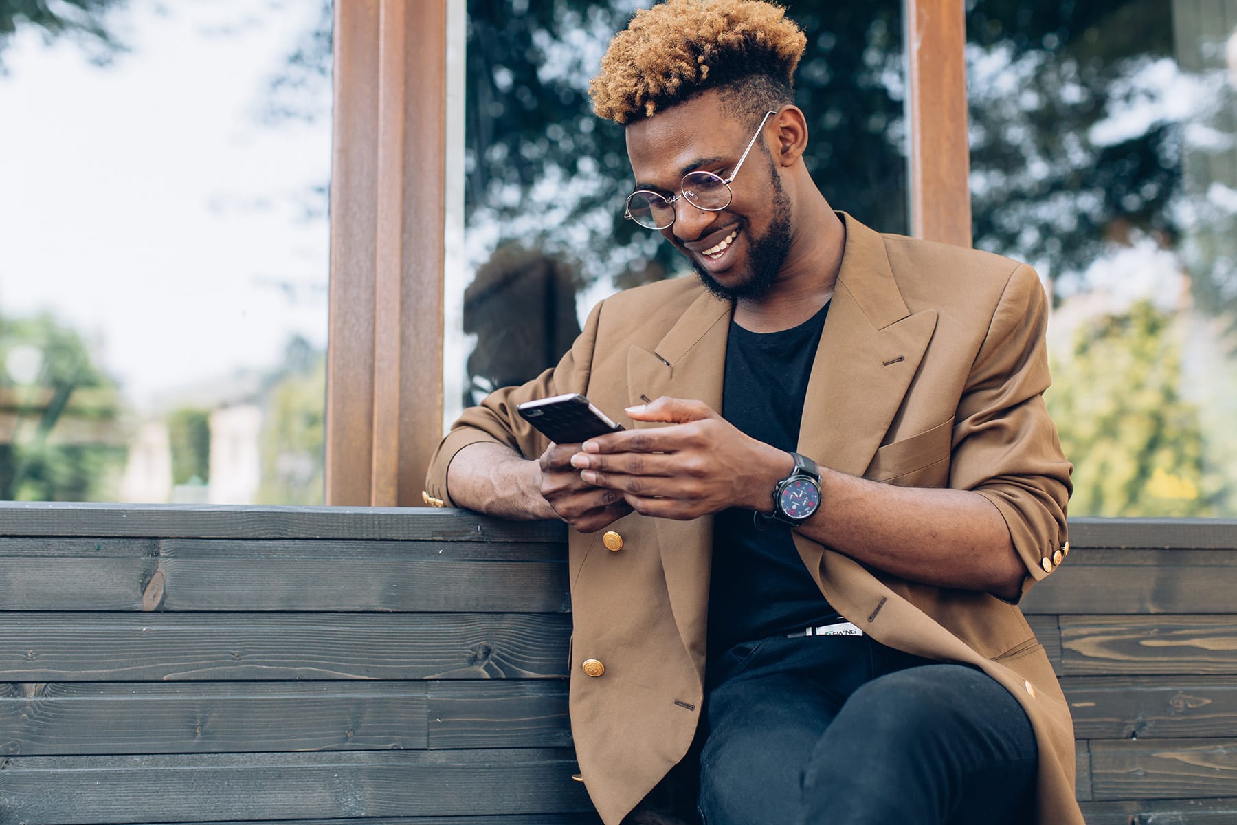 A person sits on an outdoor park bench on a sunny day, smiling contentedly while texting on their cell phone, illustrating the ease and convenience of opening a live chat with BankNewport to get banking help anytime, anywhere.