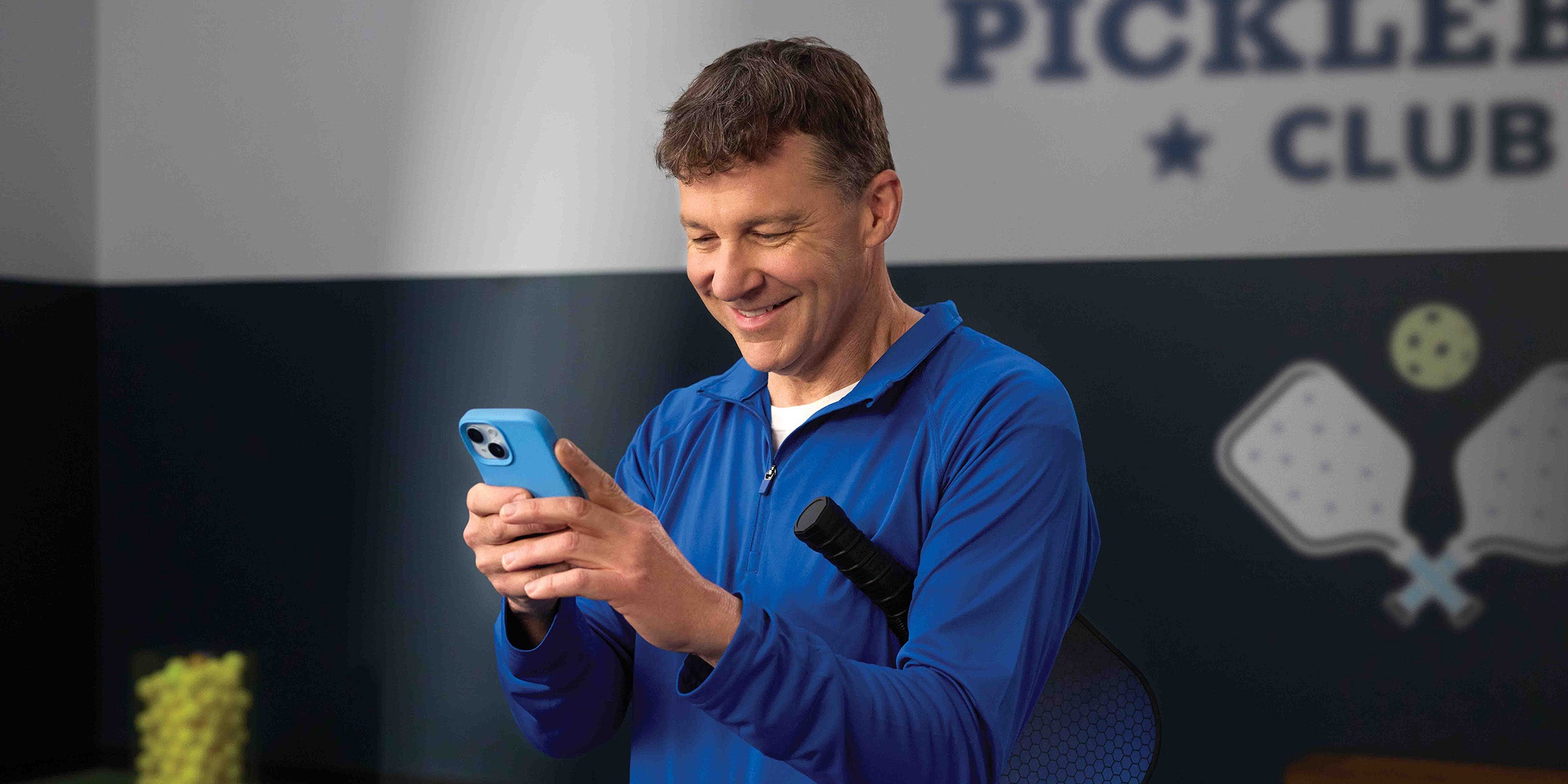 An athletic person tucks a sports racket under one arm while using both hands to interact with their mobile phone, depicting the convenience and accessibility of BankNewport's digital banking services, mobile banking tools, and digital account opening capabilities available anytime and anywhere.
