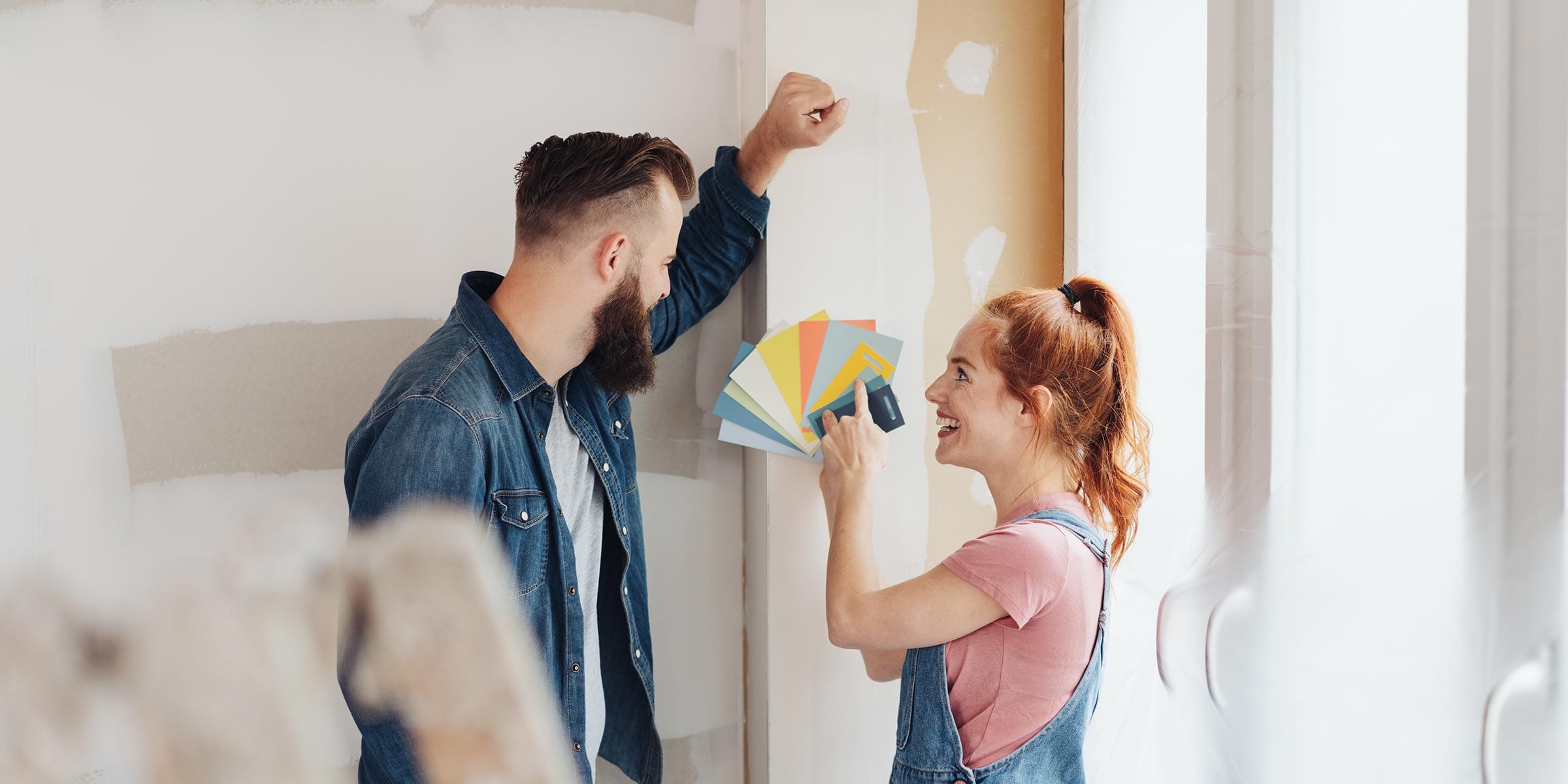 Two people happily look over paint chip color samples in a bright, sunny room with freshly painted walls, representing the home improvement projects made possible through home equity loan rates and home equity lines of credit in Rhode Island.