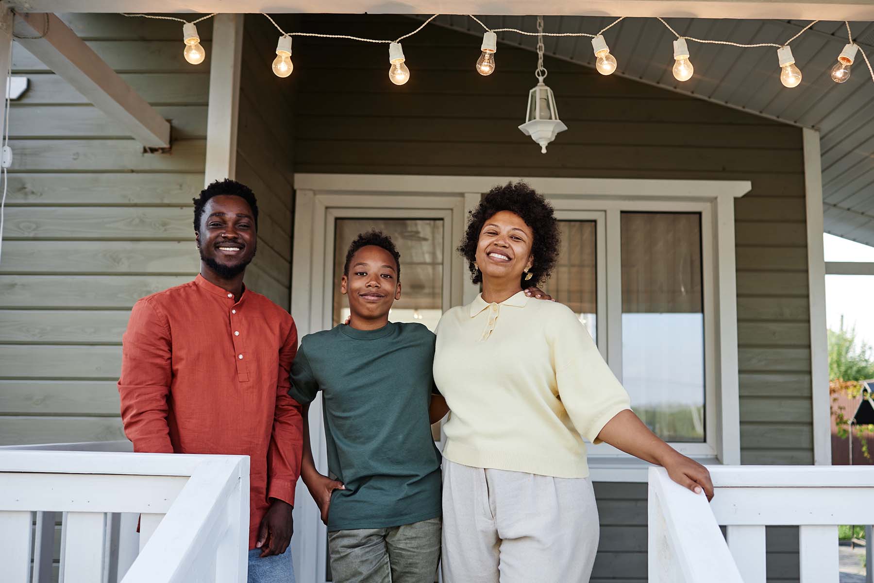 A family stands together with proud, friendly smiles at the top of the staircase leading to their home's front porch, representing the milestone of homeownership and the family life made possible through BankNewport home loans, personal home loans, and Rhode Island home loan solutions tailored to families across the state.