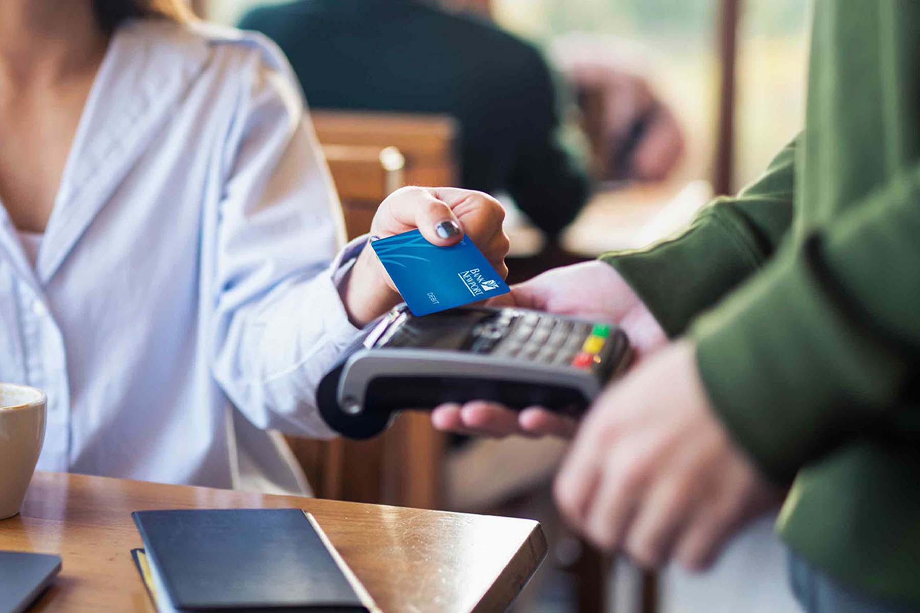 A person taps a BankNewport credit or debit card to a mobile point of service terminal at a local restaurant or coffee shop, representing local business support, the Shop401 initiative, and BankNewport's commitment to Rhode Island business and community growth.