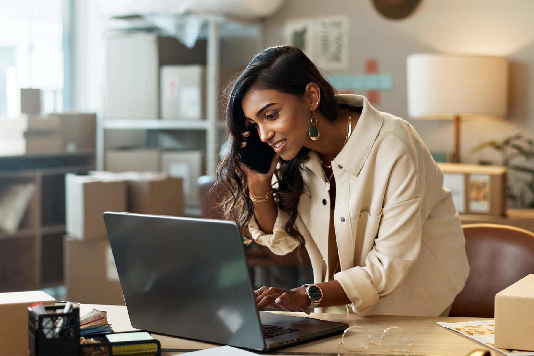A person works on a laptop and cellphone simultaneously in a clean, modern home office setting, representing the accessible, digitally enabled investment services, guided wealth portfolio management, and investment solutions available to Rhode Island investors through BankNewport from wherever they choose to work.