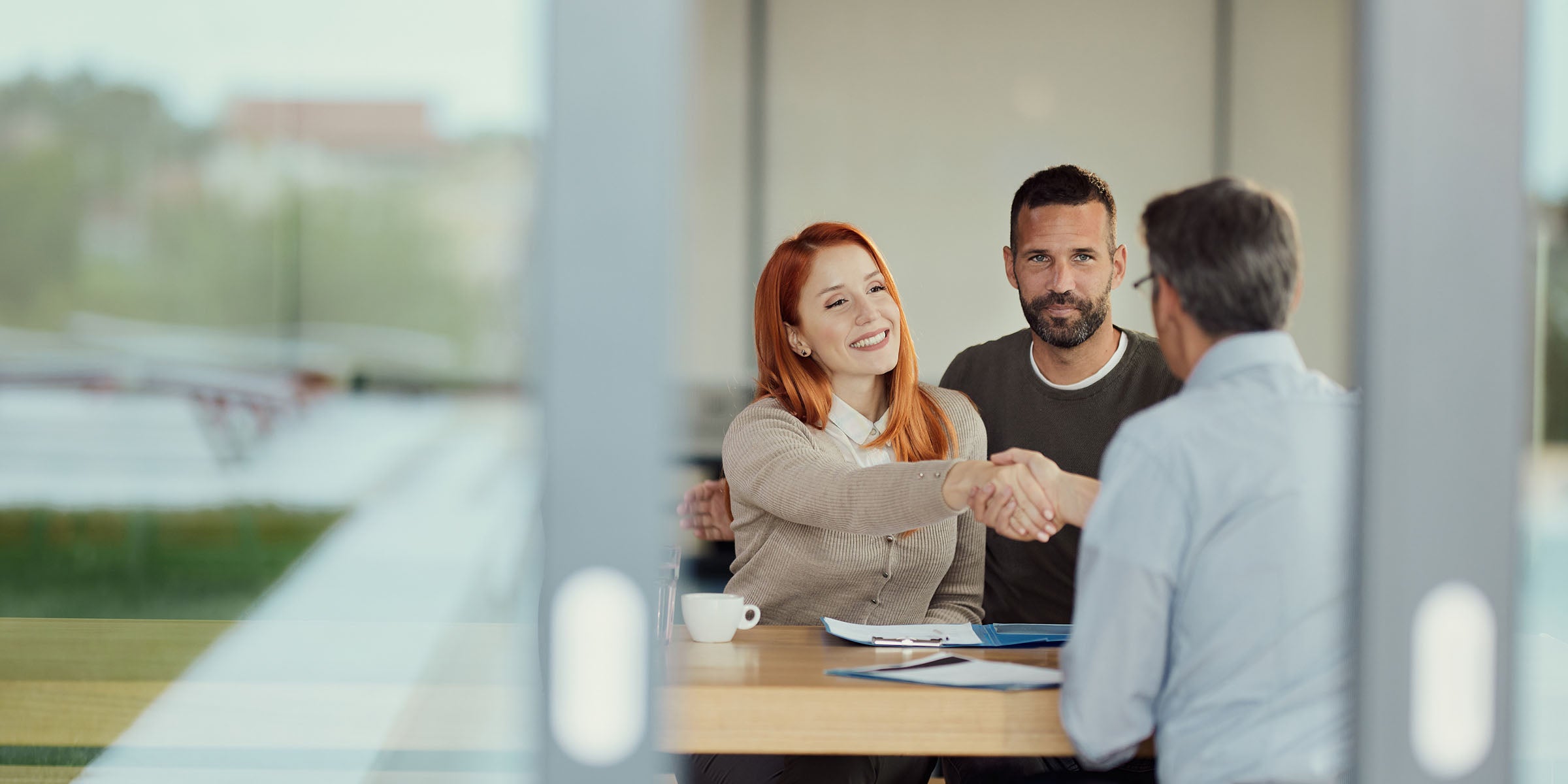 Three people share a friendly handshake across a desk during an informational meeting, representing the trustworthy, relationship-centered lending services, Rhode Island lending guidance, and personalized borrower support offered through BankNewport's full suite of RI lending services.