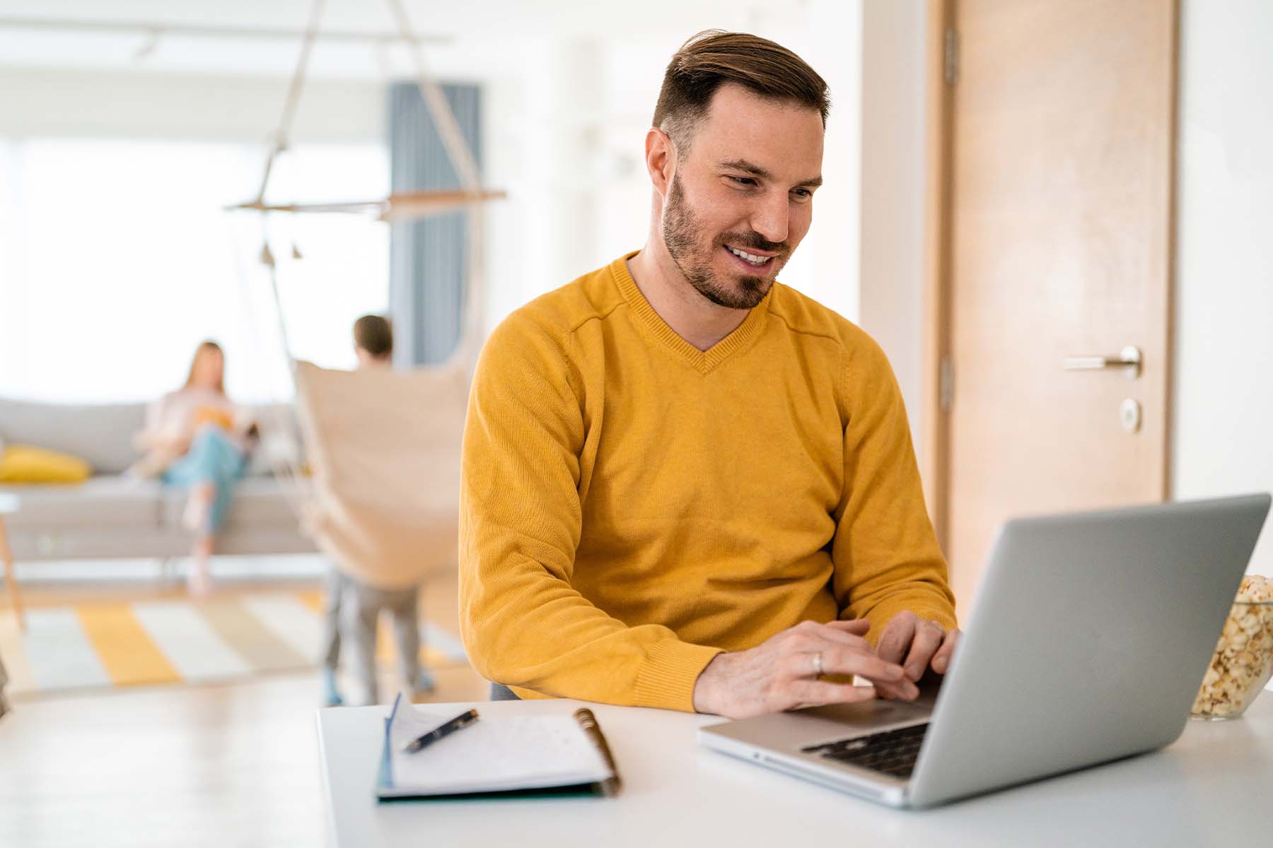 A person sits in a bright, sunlit living room working on a laptop, representing the simplicity and accessibility of opening a money market account or personal savings account online through BankNewport's digital banking platform from the comfort of home.