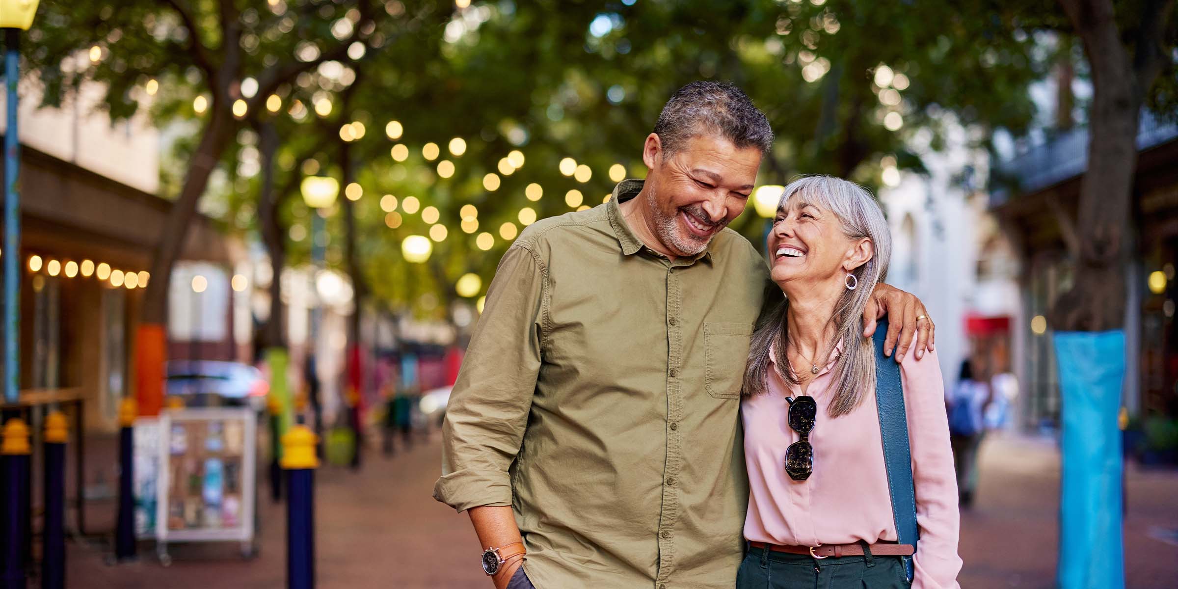 A smiling man and woman walk arm in arm through a vibrant open air market in the afternoon sunlight, representing the lifestyle, freedom, and peace of mind that high net worth banking, personalized banking, and premier banking services provide to valued clients.
