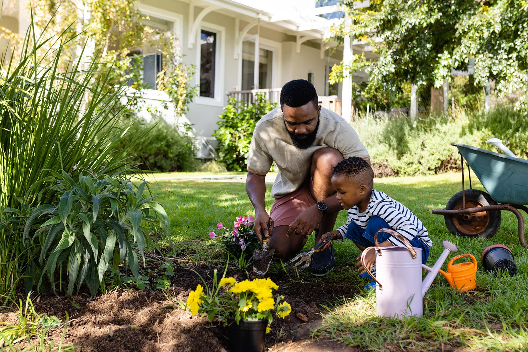 A man and a young child work side by side on simple outdoor landscaping projects on a sunny afternoon, representing the pride of homeownership and the family moments made possible by BankNewport mortgage lending in Rhode Island